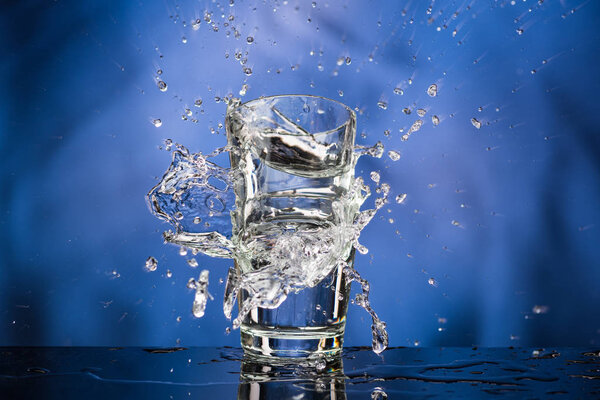 Glass with vodka and a big splash on a colored background