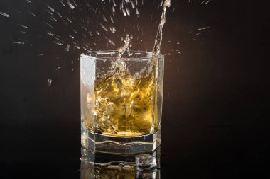 Düşen buz sıçramaları ile koyu renkli bir fotoğraf üzerinde buz ile viski bir bardak