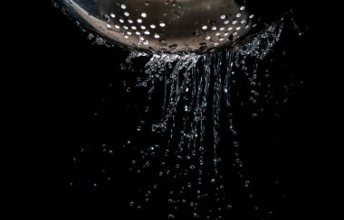 Karanlık bir arka plan üzerinde bir kevgir delikleri ile akış ve su damlaları