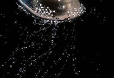 Karanlık bir arka plan üzerinde bir kevgir delikleri ile akış ve su damlaları