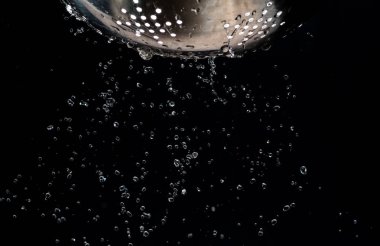 Karanlık bir arka plan üzerinde bir kevgir delikleri ile akış ve su damlaları