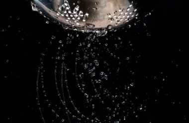 Karanlık bir arka plan üzerinde bir kevgir delikleri ile akış ve su damlaları