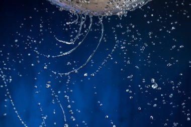 Karanlık bir arka plan üzerinde bir kevgir delikleri ile akış ve su damlaları