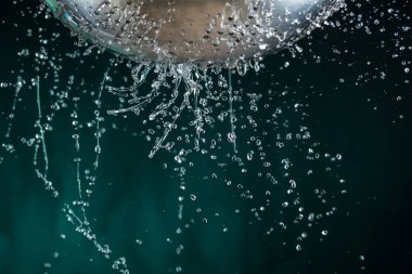 Karanlık bir arka plan üzerinde bir kevgir delikleri ile akış ve su damlaları