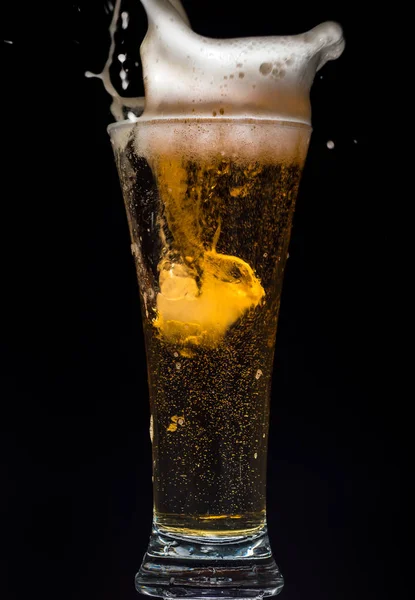 Glass of beer with foam and spray from falling ice on a turquoise green background