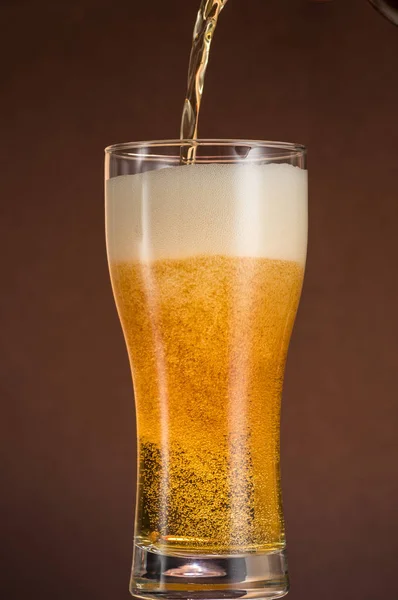 Glass of beer with foam and spray from falling ice on a turquoise green background