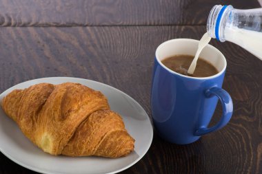 Beyaz tabakta kruvasan ve mor bardakta kahve.