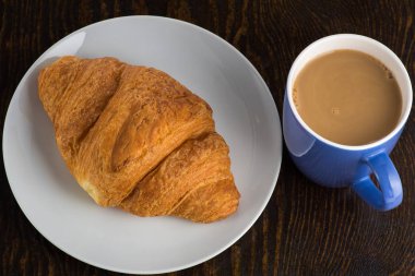 Beyaz tabakta kruvasan ve mor bardakta kahve.