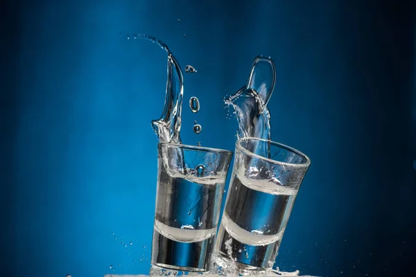 Óculos Caindo Com Vodka Spray Fundo Azul — Fotografia de Stock