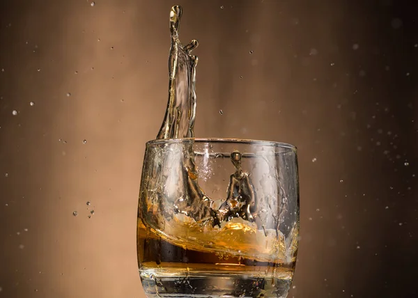 falling glass with whiskey and spray on a brown background