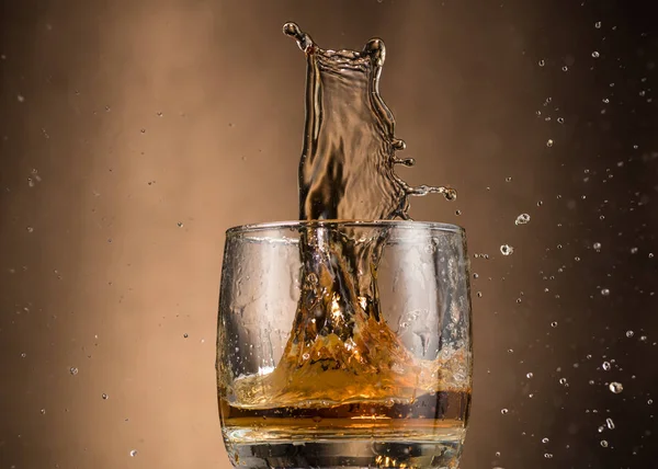 falling glass with whiskey and spray on a brown background