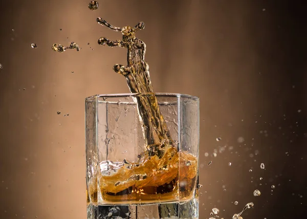 falling glass with whiskey and spray on a brown background