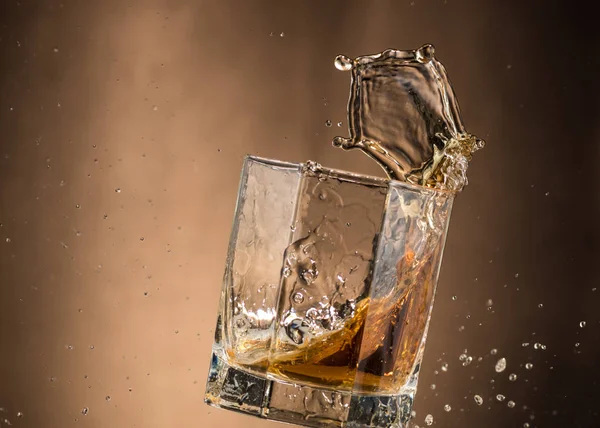 falling glass with whiskey and spray on a brown background