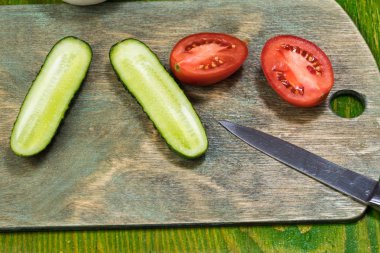 Taze sebzeler, yarım domates, salatalık, yeşil ahşap bir yüzeyde bıçakla kesme tahtasındaki soğan.
