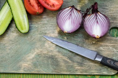 Taze sebzeler, yarım domates, salatalık, yeşil ahşap bir yüzeyde bıçakla kesme tahtasındaki soğan.