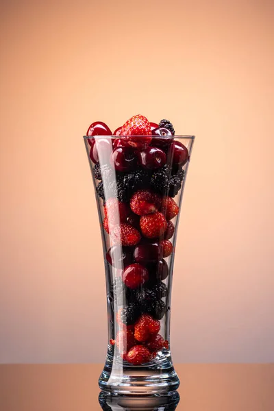mix of cherries, strawberries and mulberries in a transparent glass on a gradient background