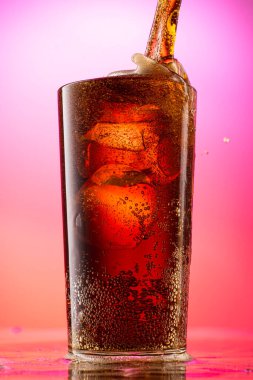 Kırmızı mor gradyan arkaplan üzerinde saf buz parçaları olan bir bardağa kola dök.