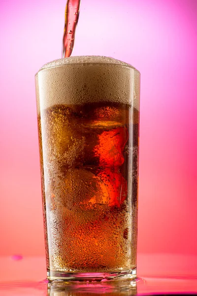 pour cola into a glass with pieces of pure real ice on a red purple gradient background