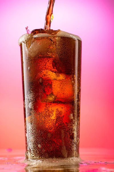 pour cola into a glass with pieces of pure real ice on a red purple gradient background