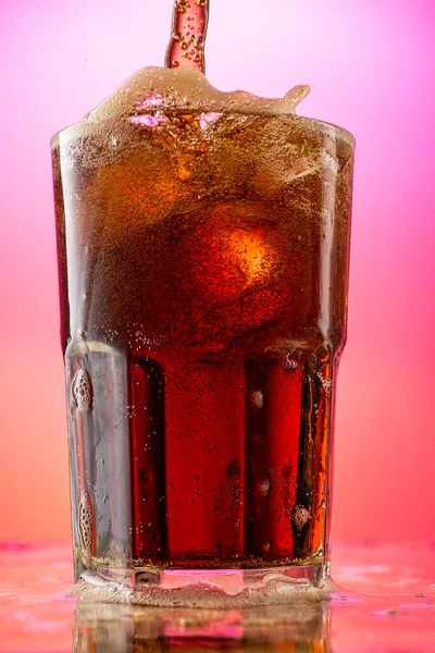 pour cola into a glass with pieces of pure real ice on a red purple gradient background