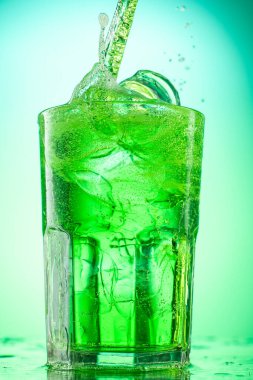 Yeşil eğimli arka planda saf buz parçalarıyla yeşil tarhun limonatasını cama dökerek.