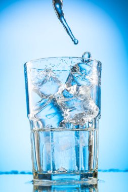Bir bardağa temiz su dökün. Mavi eğimli arka planda saf buz parçaları olsun.