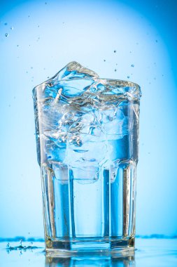 Bir bardağa temiz su dökün. Mavi eğimli arka planda saf buz parçaları olsun.