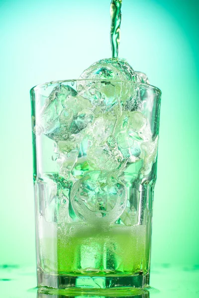 用绿色渐变背景的纯冰块把绿色的龙舌兰柠檬水倒入玻璃杯中 — 图库照片