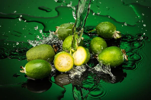 several feijoa fruits with drops and splashes of water on dark glass with gradient background and reflection