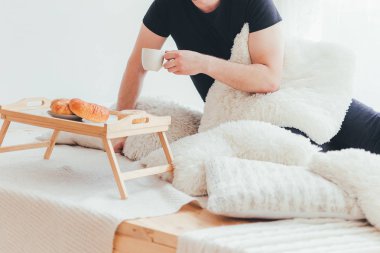 Adam bir fincan kahve tutuyor. O kahvaltı lezzetli ve taze kruvasan ile vardır. Sabah yatakta kahve.