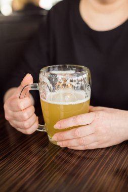 Bir kadın büyük bir bardak hafif soğuk bira tutuyor. Arkadaş grubu Toplantı.