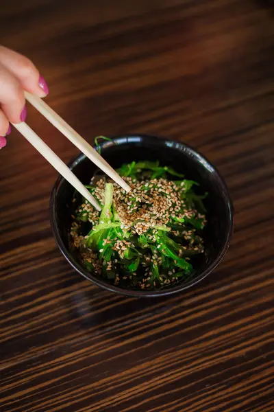 Japon yemekleri. Kız bir salata yeşil yosun susam tarafından ahşap sopa ile çalışıyor.