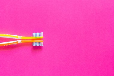 Sarı ve turuncu diş fırçaları parlak pembe bir arka plan üzerinde. Diş fırçası arka sol tarafında yer alır. Uzay kopyalayın. Yakın çekim.