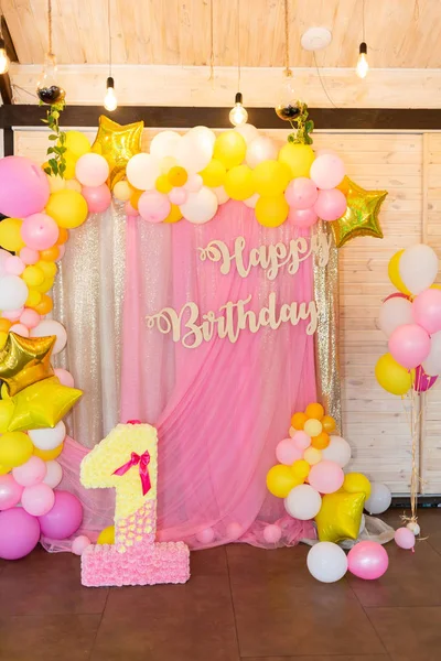 Pink, yellow and white balloons on a soft pink background. Inscription Happy Birthday. The decor for the celebration of the first birthday of the baby.