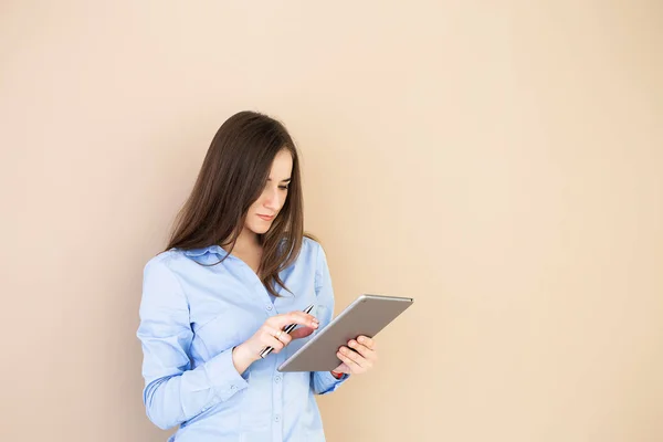 Bej renkli bir arka plan üzerinde izole bir tablet kullanan bir iş kadın portresi. Kadın bir tablet ve kalem ellerinde tutuyor.