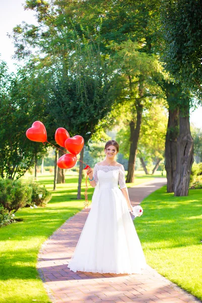 Güzel mutlu gelin onun el balonları bir kalp şeklinde tutar. Yaz düğün parkta. Yeşil ve güzel civarındadır.