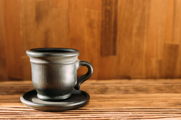 Black clay mug with coffee on a white background. a clay cup of black color on a wooden table. Close up. side view