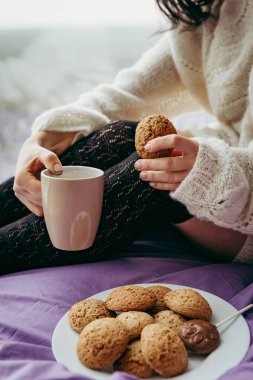 çay kahve içme ve pencerenin yanında otururken kurabiye yemek genç esmer kadın 