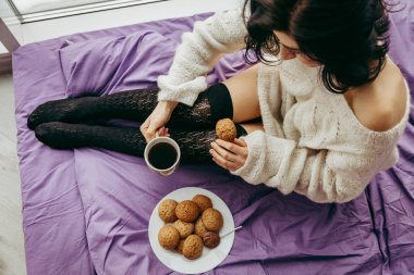 çay kahve içme ve pencerenin yanında otururken kurabiye yemek genç esmer kadın 