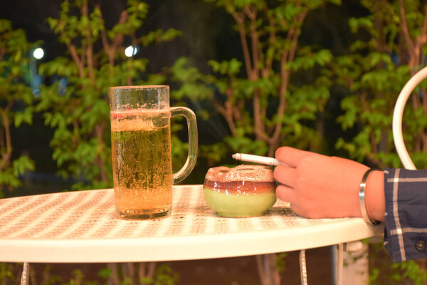 A glass of cool beer on the table, beside a glass there is hand 