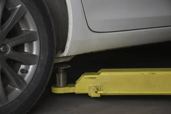 Kirli beyaz araba değişiklik tekerlekleri onarım istasyonu için sarı Hidrolik Asansör arabayla kaldırdı.