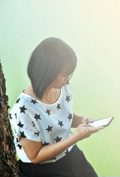 A woman in star-white shirt is checking her smartphone with white flare.