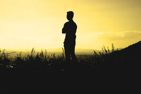 A black silhouette of a man is crossing one's arm and standing on a hill in the morning or evening