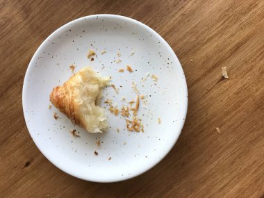 Ahşap masada beyaz çanak kruvasandan bir ekmek kırıntısı.