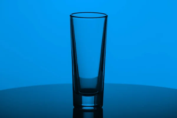 Verre vide pour vodka sur une surface réfléchissante sur fond bleu. Plats pour alcool — Photo