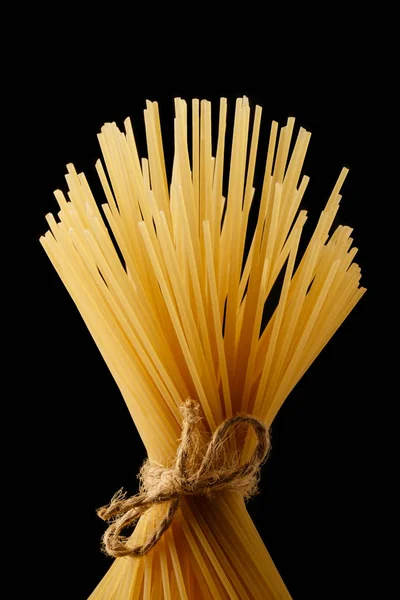 スパゲッティの束は、ロープで縛られて。黄色のイタリアン パスタ。長いスパゲッティ。黒の背景に分離 — ストック写真