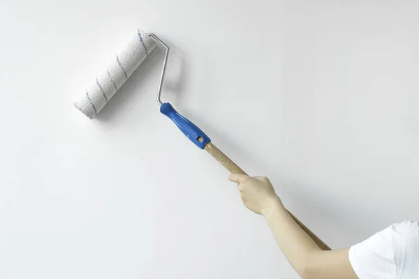 Una mano con un rodillo pinta la pared con pintura blanca. Pared de pintura a mano del decorador con rodillo —  Fotos de Stock