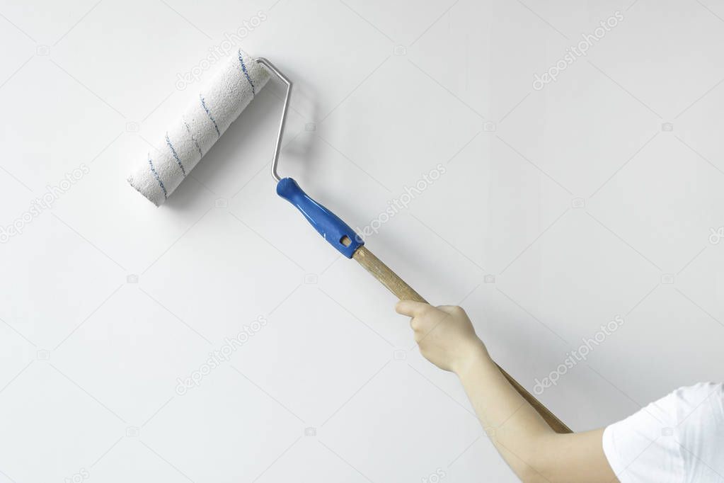 A hand with a roller paints the wall with white paint. Decorator's hand painting wall with roller