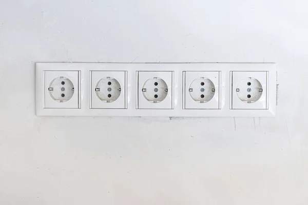 Cinco tomas de corriente blancas con marco en la pared blanca como fondo —  Fotos de Stock