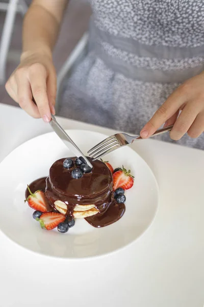 Café da manhã com amigos em um café de verão ao ar livre. Na mesa estão panquecas de sobremesa com chocolate e mirtilo no topo. Mãos na armação com talheres . — Fotografia de Stock